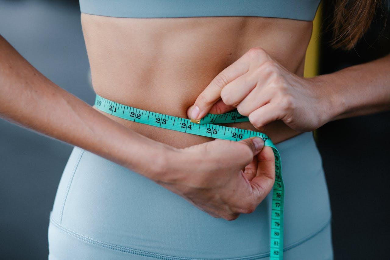 why-choose-us Close-up of a woman measuring her waist with a tape, representing fitness, health, and weight loss.
